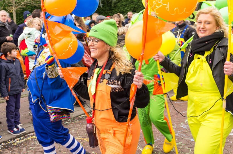 Cheerful lady in orange overall with green hat holds a stick with orange balloons royalty free stock images