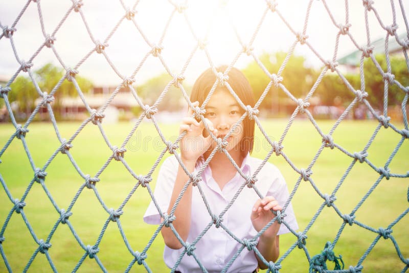 Cute portrait of innocent Asian girl teen student stand behind the rope net looking camera with sunshine. Asia Thai people stock photos