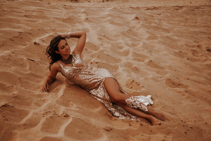 Full length portrait of woman in expensive gold dress posing in desert, lying on the sand at the sunset royalty free stock images