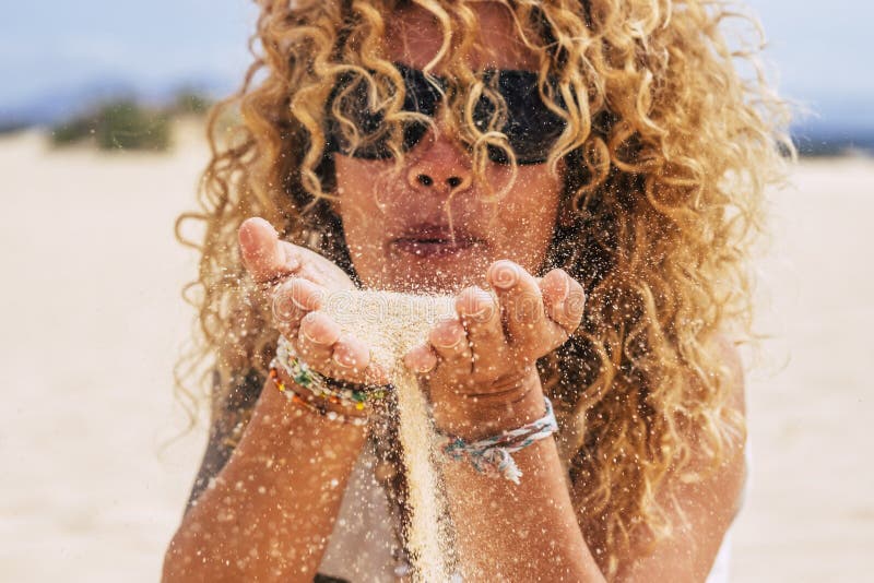 People in summer holiday vacation concept - young pretty curly blonde woman blow sand at the beach in a sunny day - focus on hands royalty free stock photo