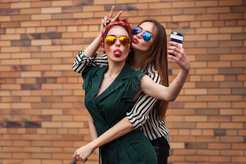 Two young sexy fashion women posing for selfie and laughing with tonque. Lifestyle portrait on street city background stock image