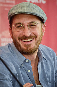 Darren Aronofsky kneeling while holding a microphone